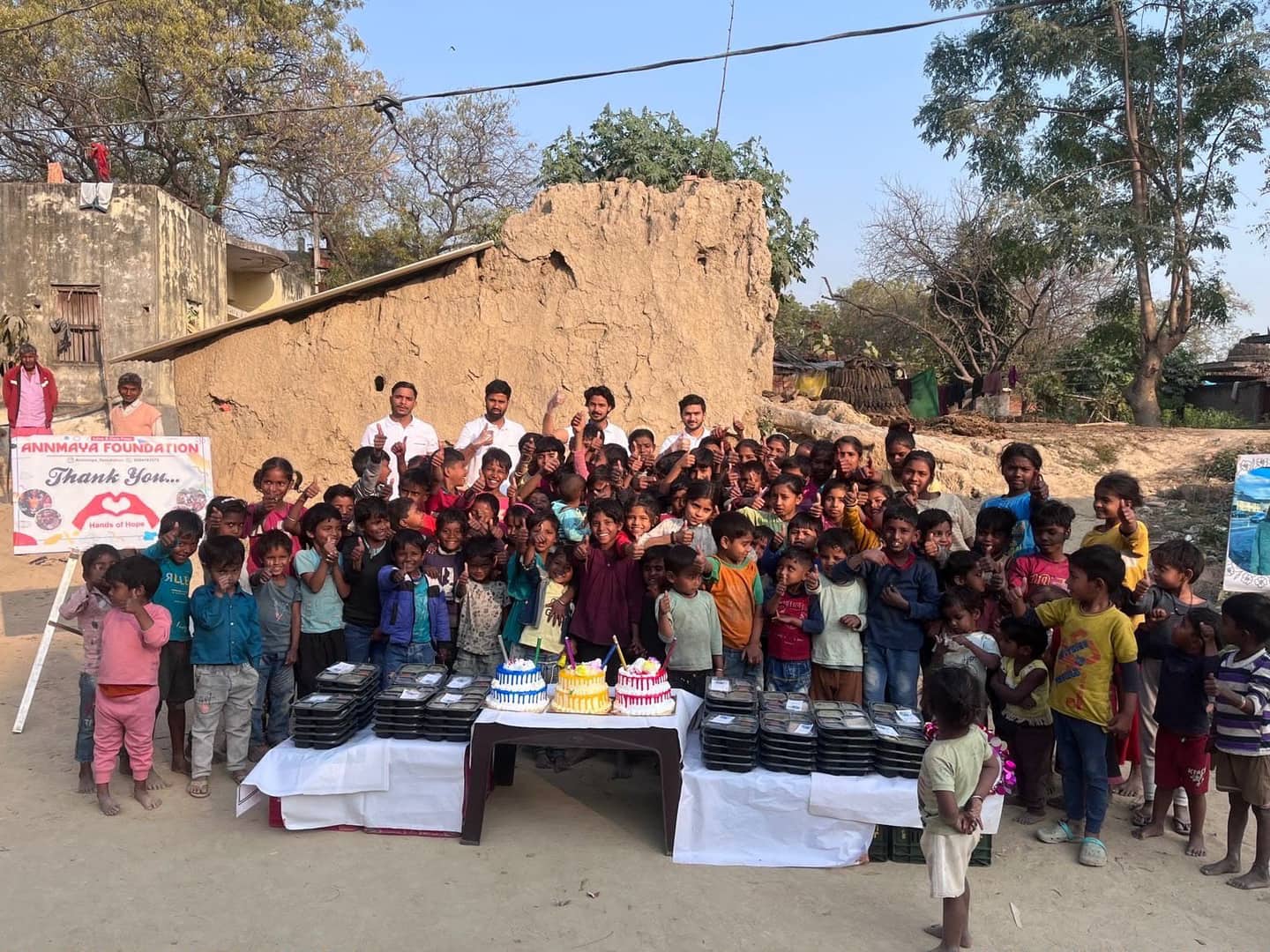 Children and Annmaya volunteers gathered around birthday cakes and meal trays at a distribution event