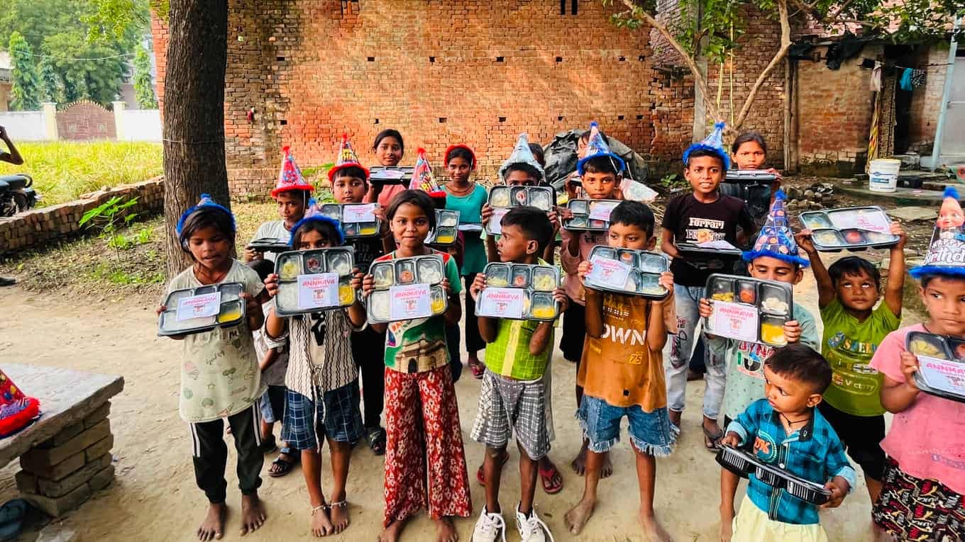 An Annmaya volunteer handing meal trays to children in front of a thank-you banner