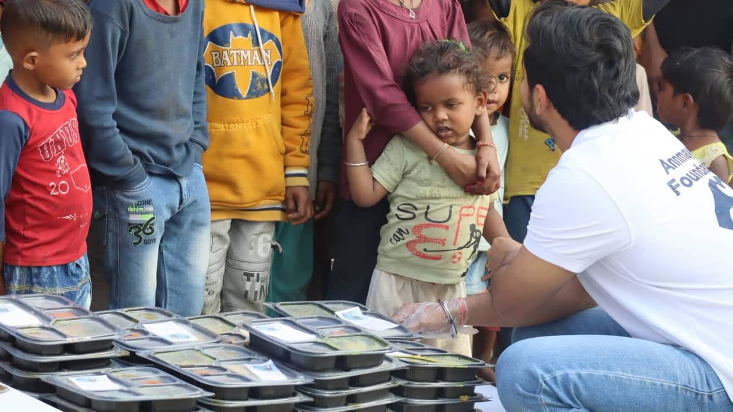 An Annmaya volunteer crouching to hand meal trays to a group of children