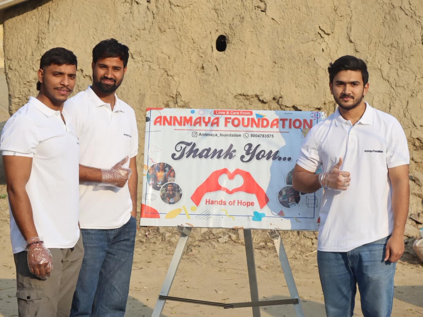 Three Annmaya Foundation volunteers standing beside the foundation’s thank-you banner